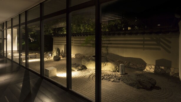A corridor with large windows overlooking a landscaped garden area with rocks and a stone wall. - Sapporo Grand Hotel (Sapporo)