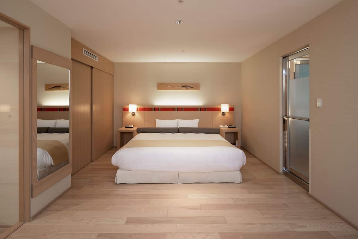 Une chambre d’hôtel avec un grand lit, des tables de chevet, un miroir et une armoire.