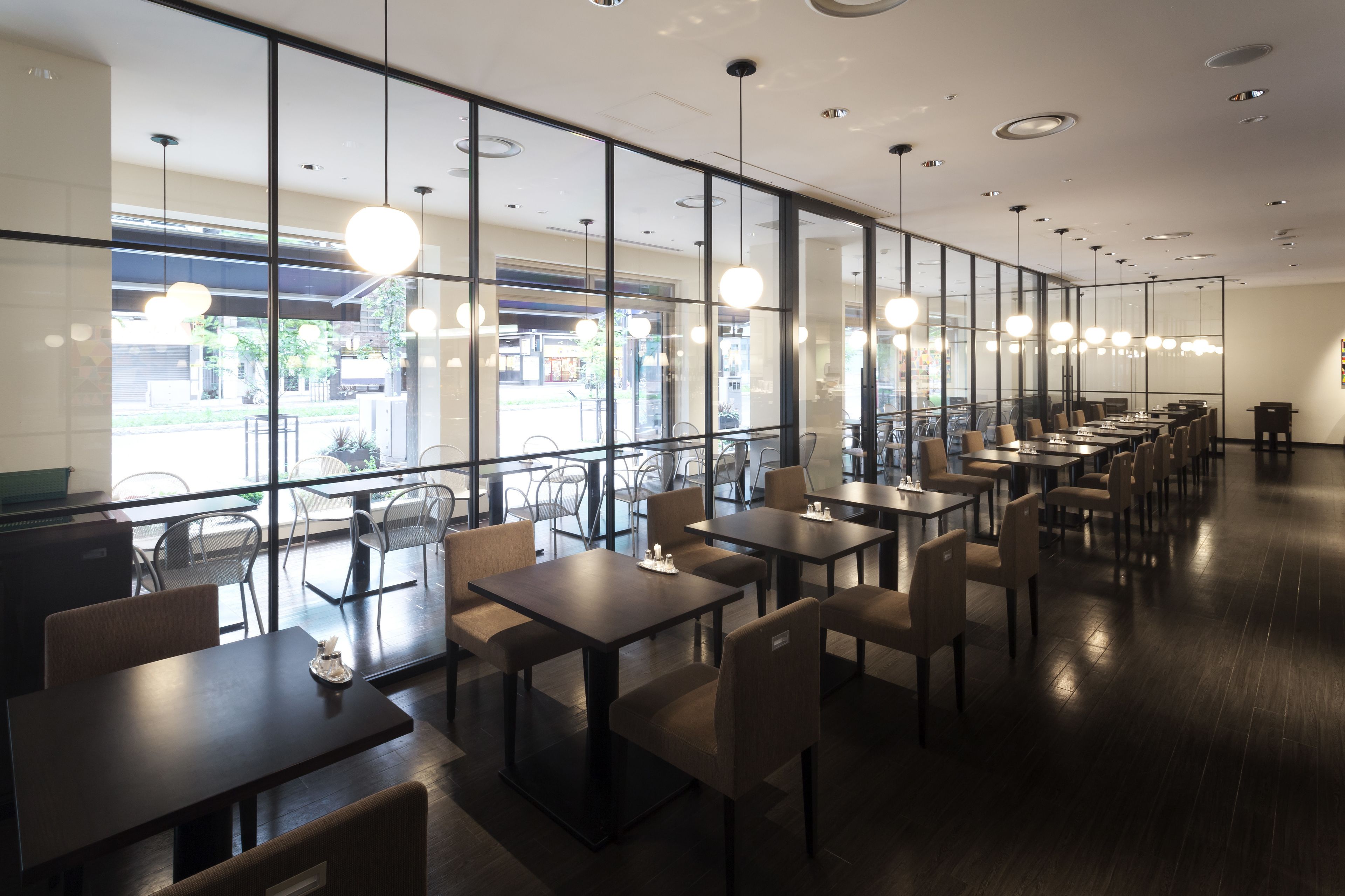 Ein modernes Restaurant mit langen Tischen und Stühlen, großen Fenstern und Pendelleuchten.
