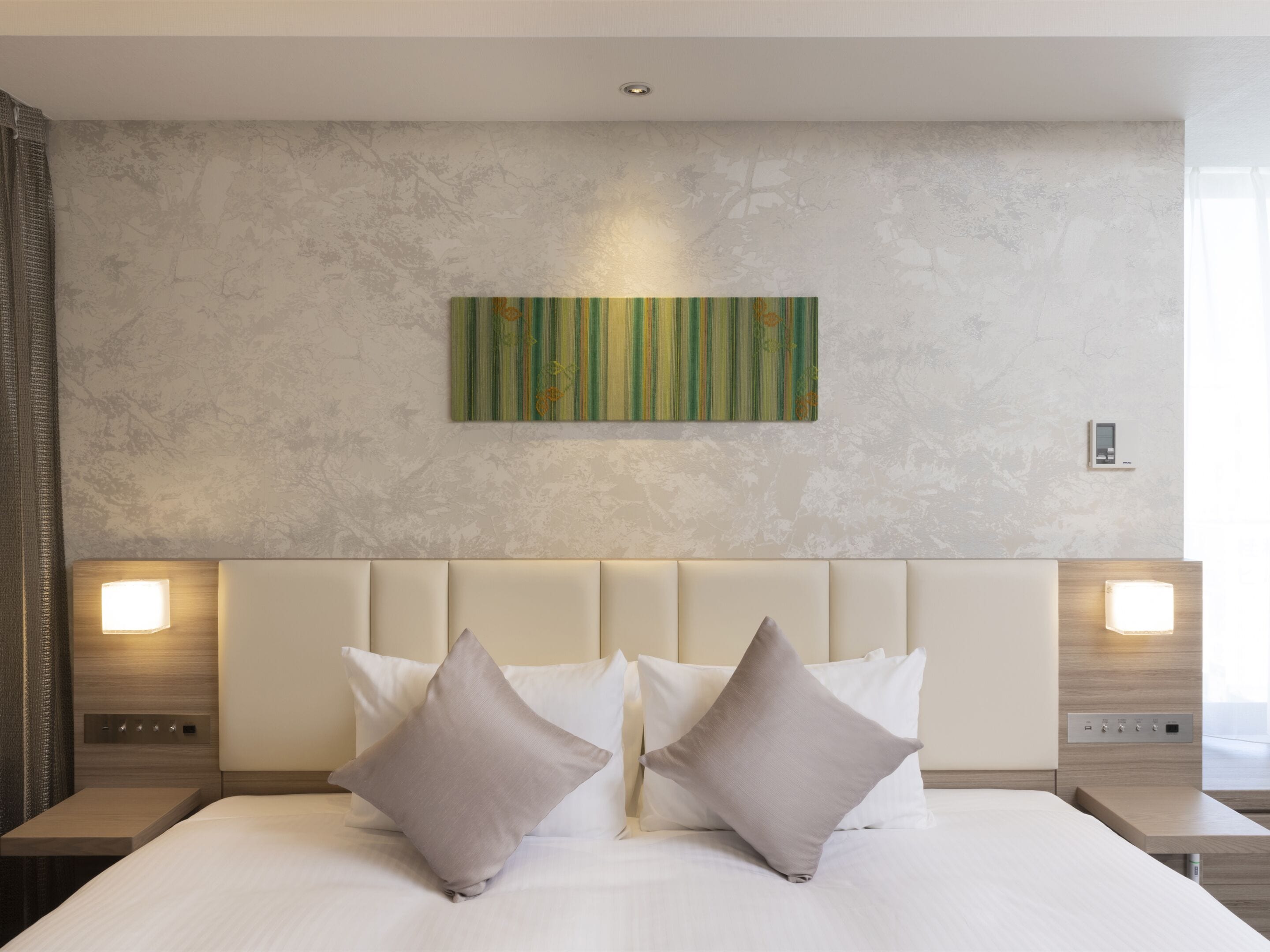 A hotel room with a large bed, two bedside tables, a wall-mounted light, and a decorative panel.