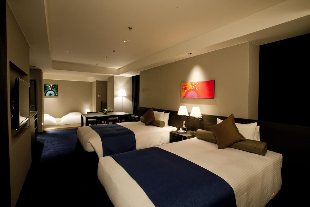 Une chambre d’hôtel avec deux lits, un bureau, une chaise, une télévision et un tableau au mur.