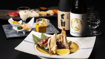 Una mesa de comedor con una botella de sake, una copa y diversos platos.