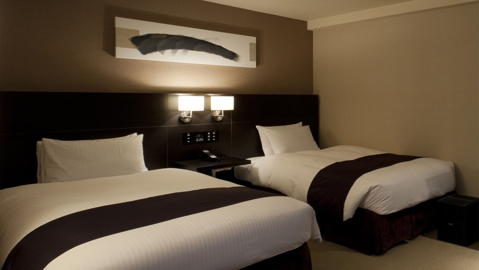 Une chambre d’hôtel avec deux lits, une table de chevet avec un téléphone et un luminaire fixé au mur.