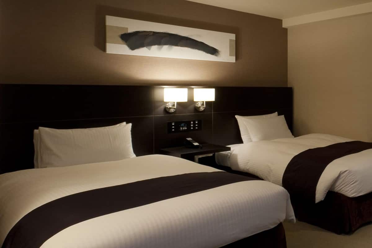 Une chambre d’hôtel avec deux lits, une table de chevet avec un téléphone et un luminaire fixé au mur.