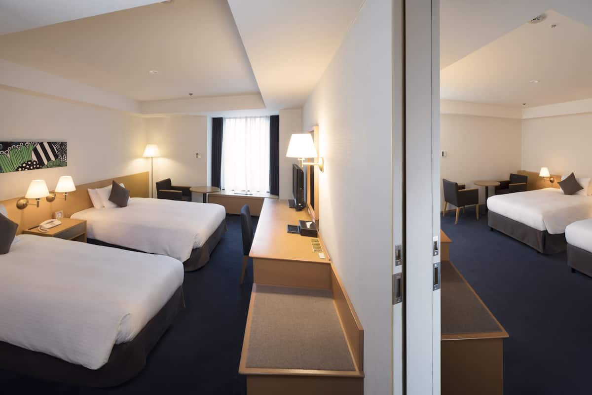 Une chambre d’hôtel avec deux lits, un bureau, une chaise, une télévision et une fenêtre avec des rideaux.