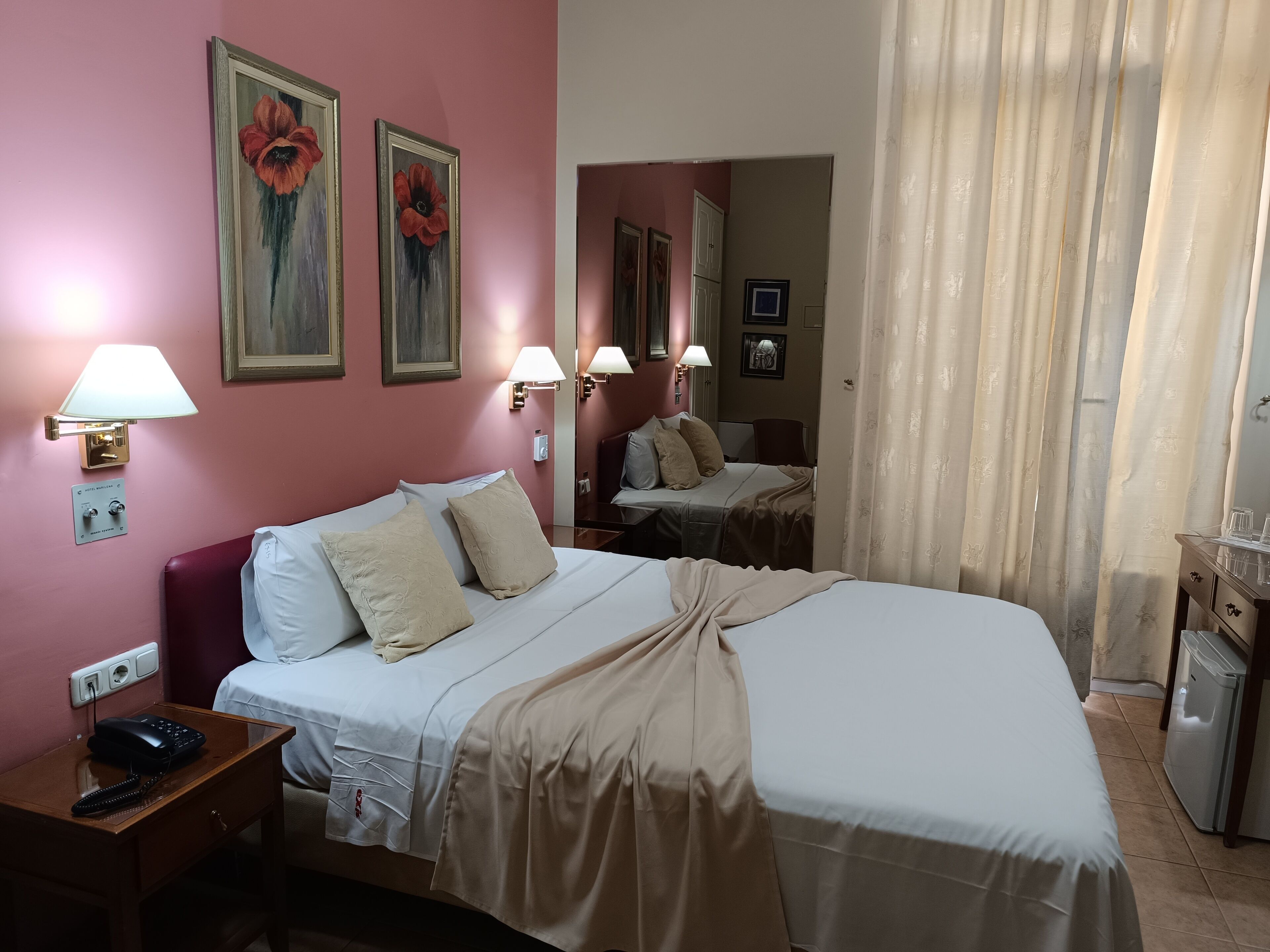Habitación de hotel con cama, lámparas de noche, mesita de noche, teléfono y espejo.