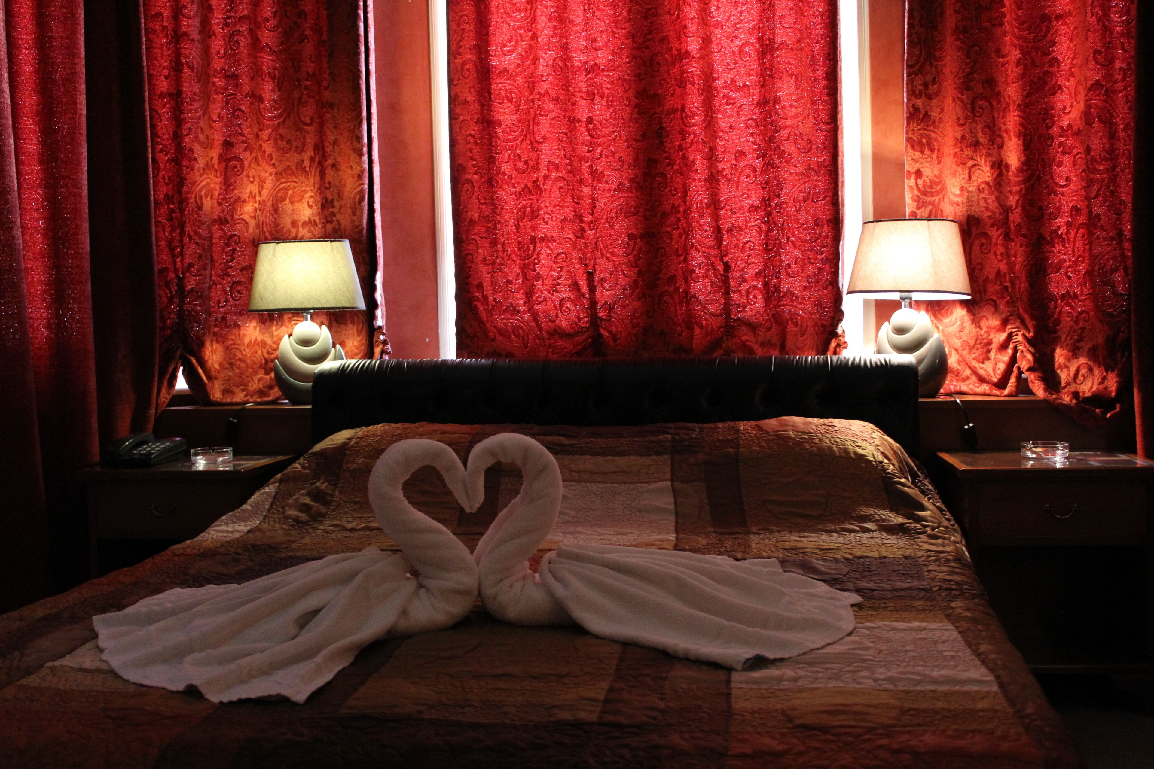 Habitación de hotel con cama, cortinas rojas, dos lámparas de noche y una decoración de toallas con forma de cisne.