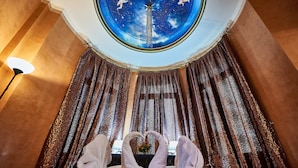 A room with a view of the sky through a circular window, a bed with two towels shaped like swans, and a lamp on the left. - Exis Boutique Hotel (Athens)