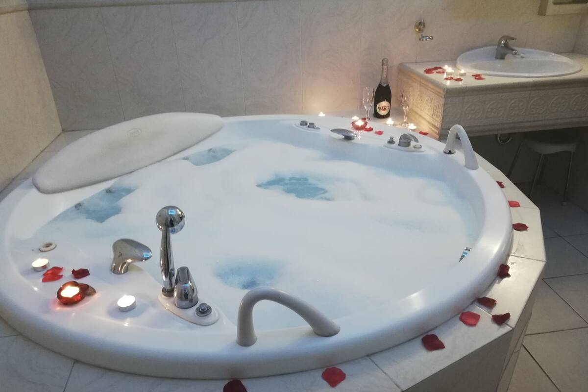 A bathtub with rose petals and candles, a bottle of champagne, and a small sink with a mirror.