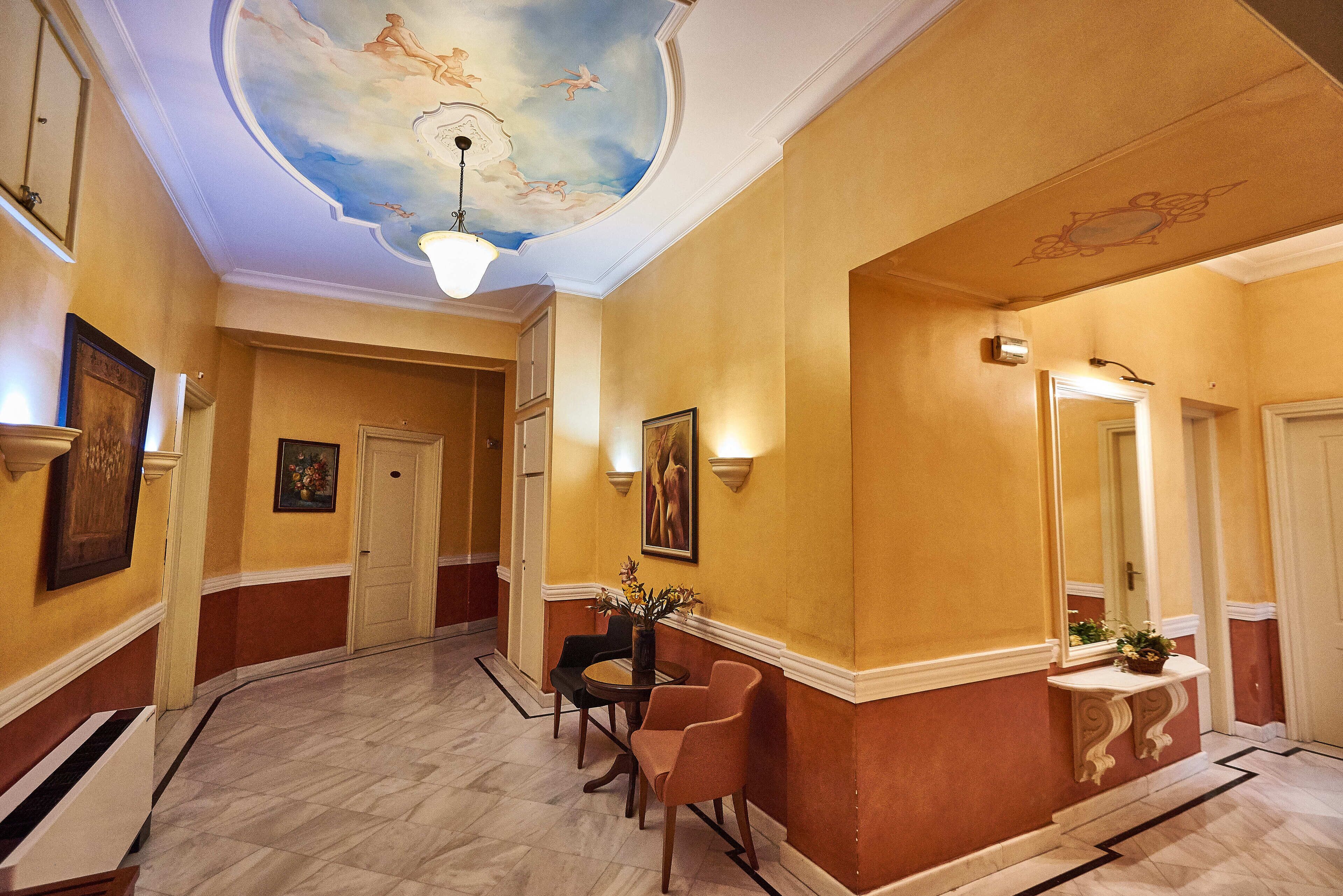 A hallway with a marble floor, a round table with chairs, a vase with flowers, and framed artwork on the walls.