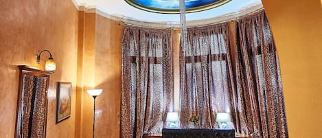 Una habitación de hotel con techo curvo, cama con edredón estampado, escritorio con lámpara y un espejo grande.