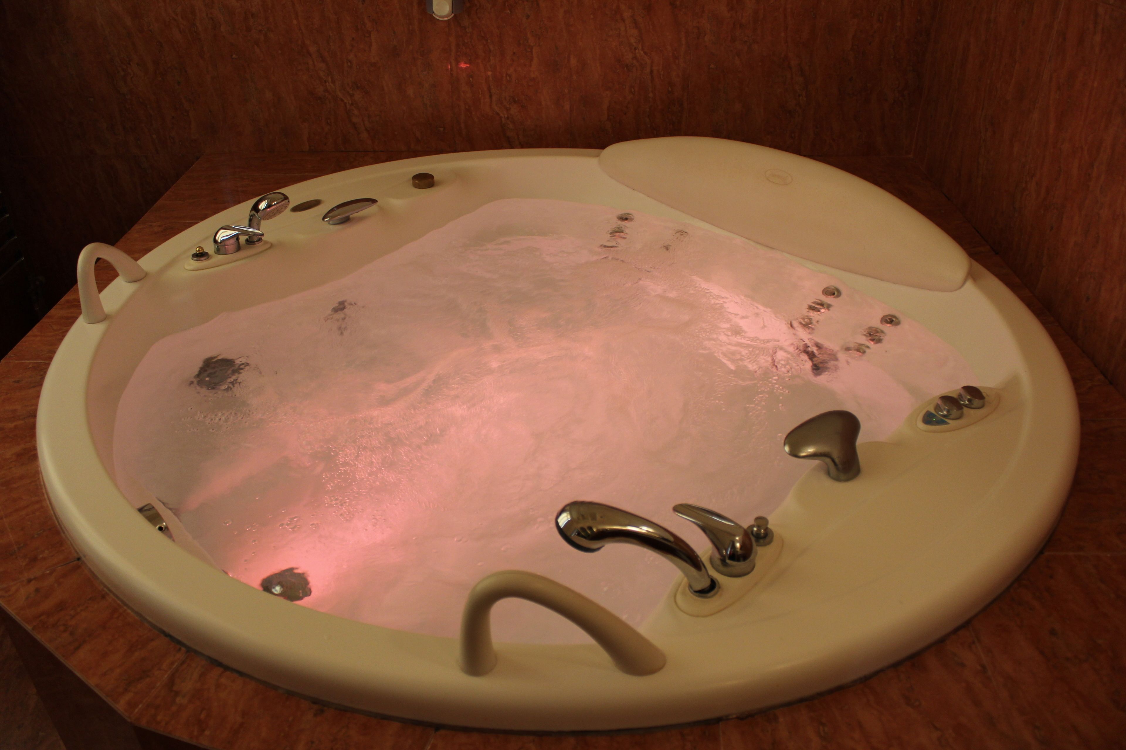 A bathtub with a built-in seat and multiple faucets.