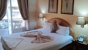 A neatly made bed with a towel arrangement, two wall-mounted lamps, and framed floral artwork. - Exis Boutique Hotel (Athens)