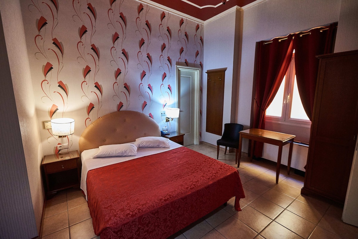 A hotel room with a bed, nightstands, a desk, a chair, and a window with curtains.