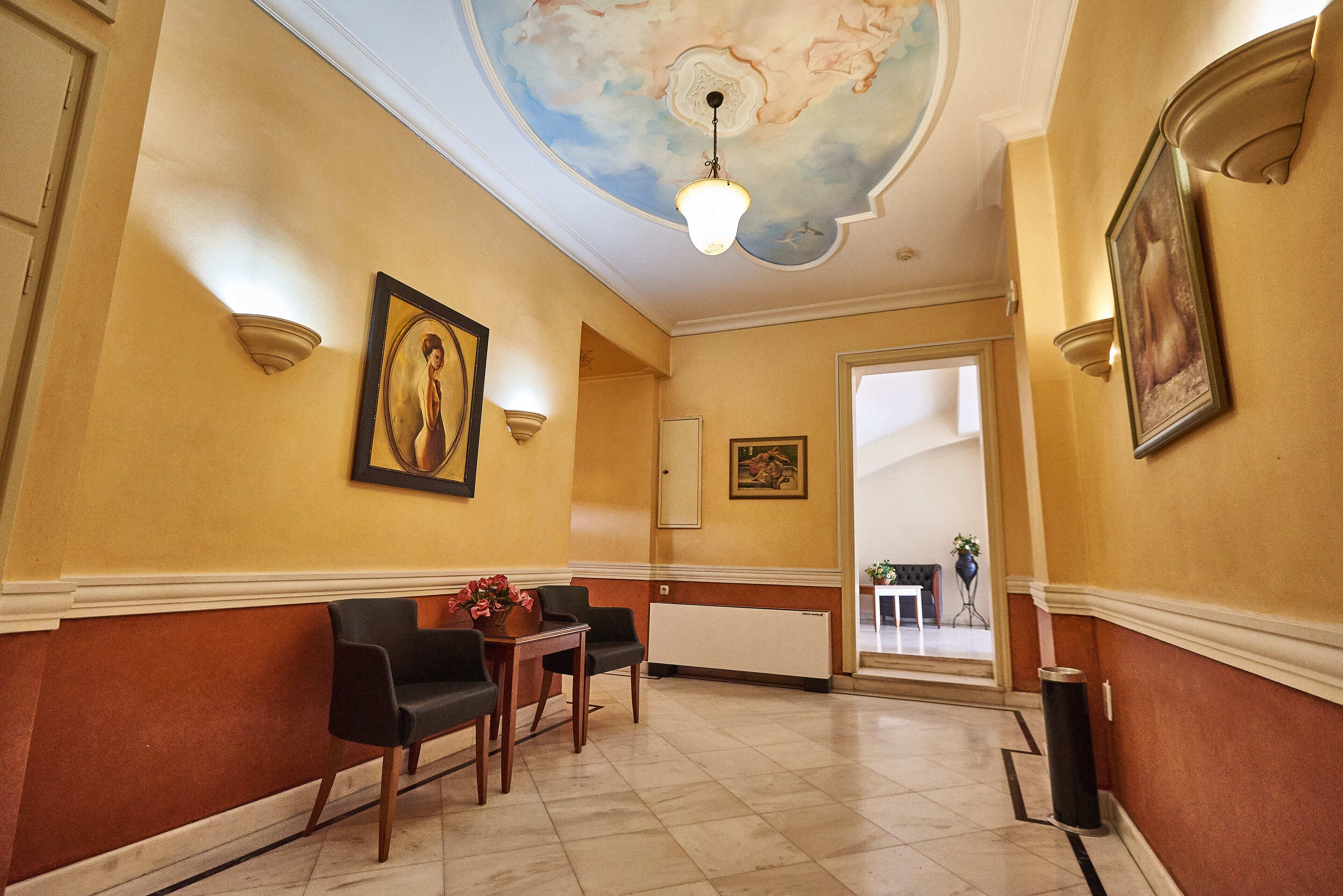 Een lobby met een marmeren vloer, een receptiebalie, twee zwarte stoelen, een tafel met bloemen en een plafond met een schilderwerk.