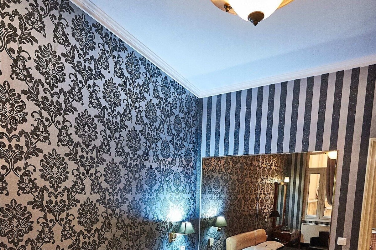 A hotel room with a large bed, a nightstand, a lamp, a mirror, and a striped wall.