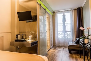 A hotel room with a bed, a desk with a coffee maker, a TV, a balcony with a view, and a chair. - District République (Paris)