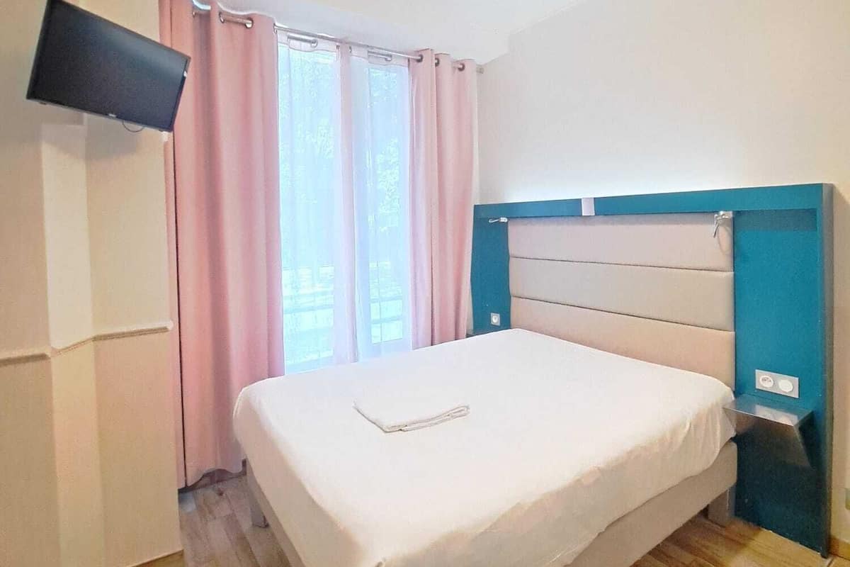 A bedroom with a bed, a TV mounted on the wall, and a window with curtains.