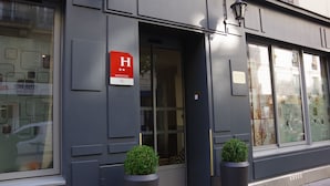 Um edifício moderno com uma grande janela de vidro, uma porta com uma placa vermelha e duas plantas em vasos.
