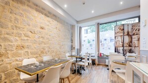 Um café moderno com paredes de pedra, piso de madeira e cadeiras brancas. Mesas dispostas para acomodar clientes.