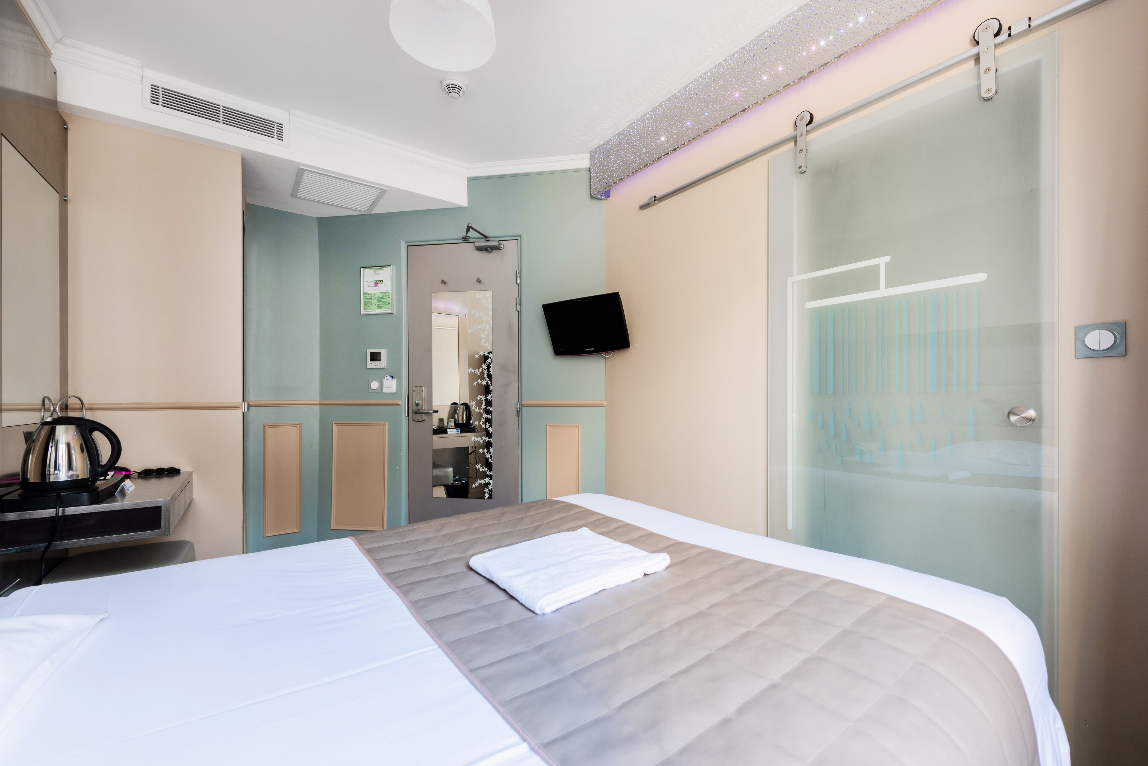 Ein Hotelzimmer mit Bett, Wandfernseher, Duschbereich und einer Küchenzeile.