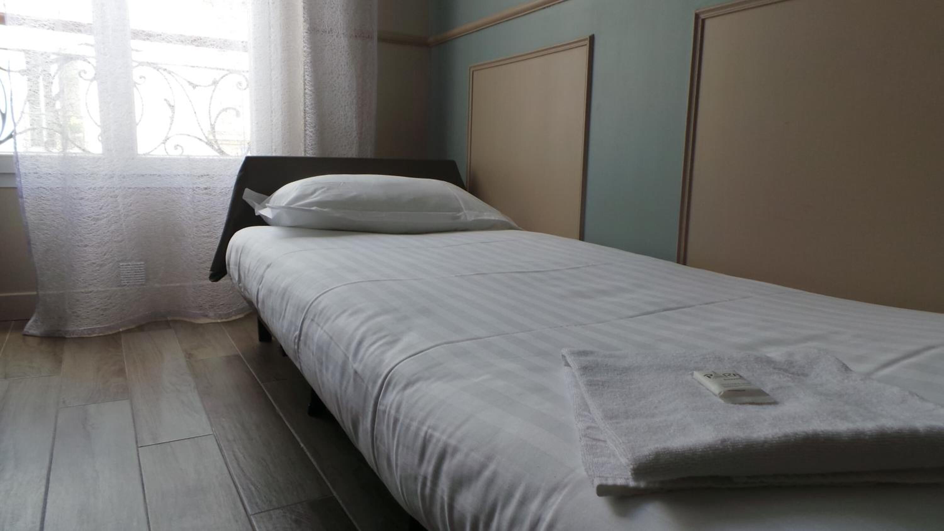 Un letto singolo con materasso e cuscino bianchi, una testiera in legno e una finestra con tenda bianca.