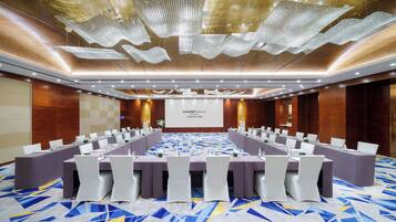 Un salón de conferencias con una larga mesa, sillas blancas y una pantalla de presentación.