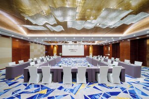 Un salón de conferencias con una larga mesa, sillas blancas y una pantalla de presentación.
