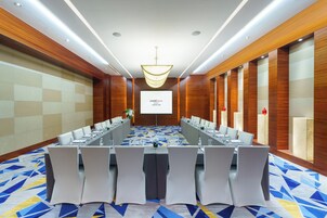 A conference room with a long table, white chairs, and a projector screen.