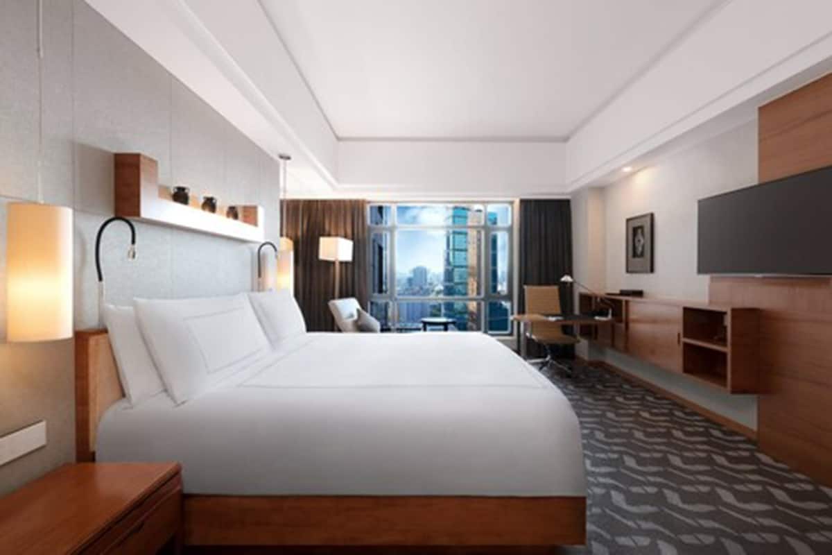 Quarto de hotel com uma cama grande, uma escrivaninha, uma cadeira, uma televisão e uma janela com vista para a cidade.