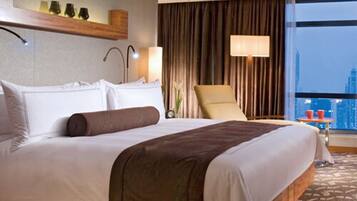 A hotel room with a large bed, a chair, a lamp, and a view of the city.