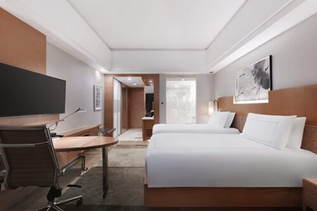 Quarto de hotel com cama, escrivaninha, cadeira e televisão.