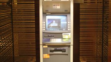 A self-service kiosk with a digital screen, card reader, and cash dispenser, located in a room with patterned flooring and wooden paneling.
