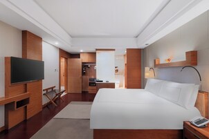 Habitación de hotel con una cama grande, televisor montado en la pared, escritorio con silla y baño visible a través de una puerta abierta.