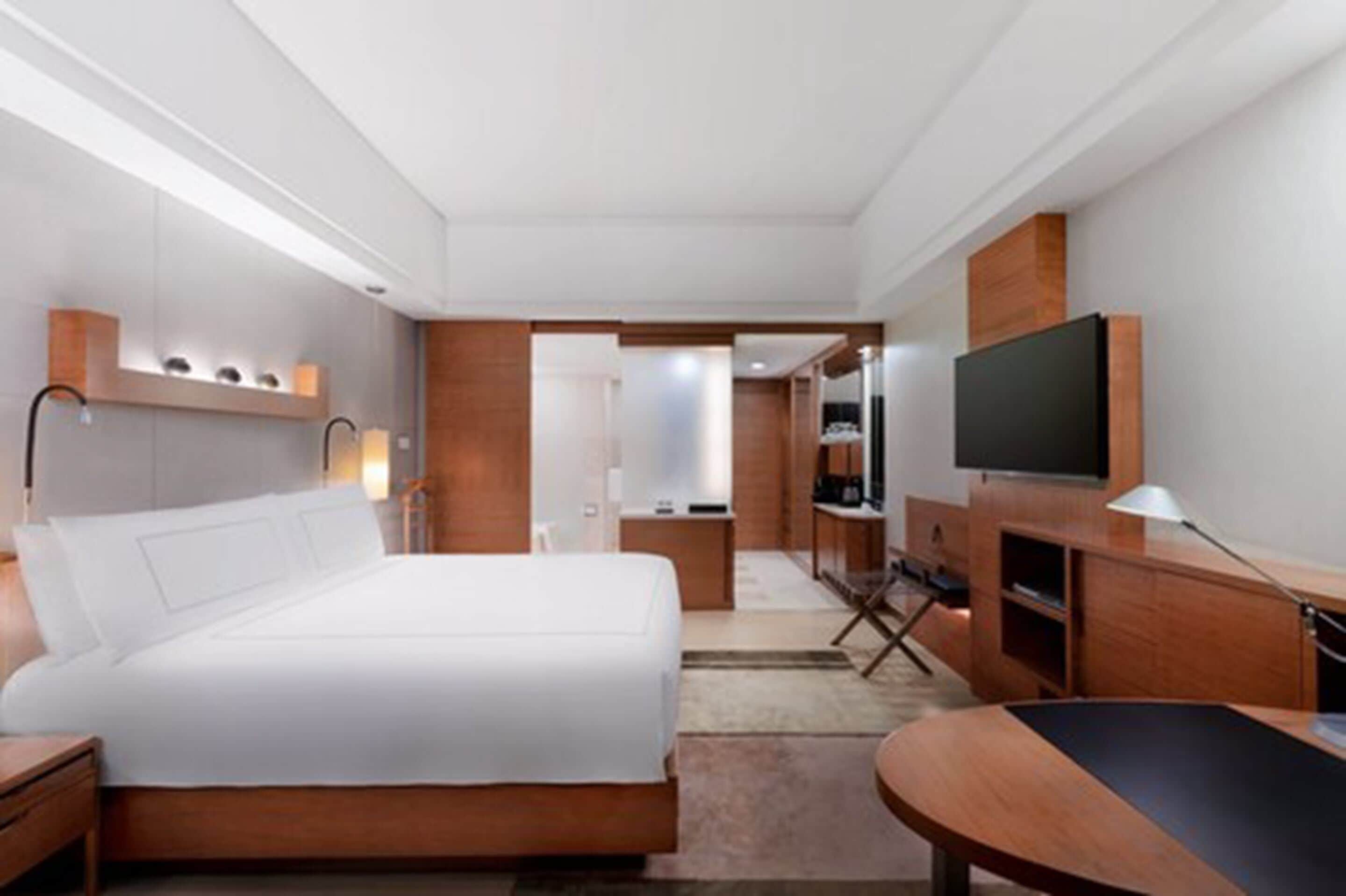 A modern hotel room with a large bed, a desk, a television, and a seating area.