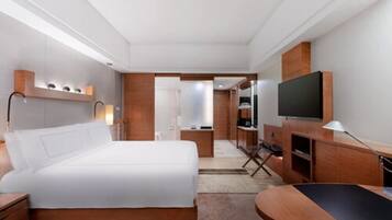 A modern hotel room with a large bed, a desk, a television, and a seating area.