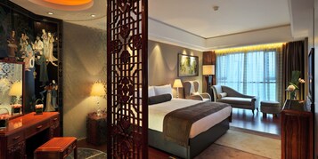 A hotel room with a large bed, a desk with a lamp, a chair, and a decorative screen.