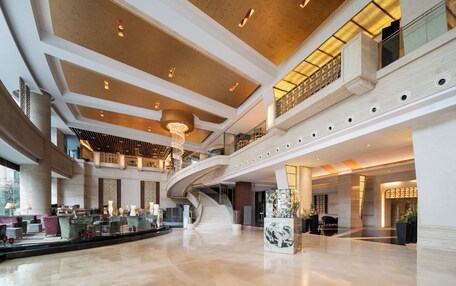 A spacious lobby with a curved staircase, a large chandelier, and a marble sculpture.