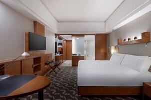 A hotel room with a large bed, a desk with a chair, a television, and a small kitchenette.