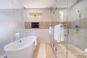 A modern bathroom with a freestanding bathtub, a glass-enclosed shower, and a flat-screen TV mounted on the wall.