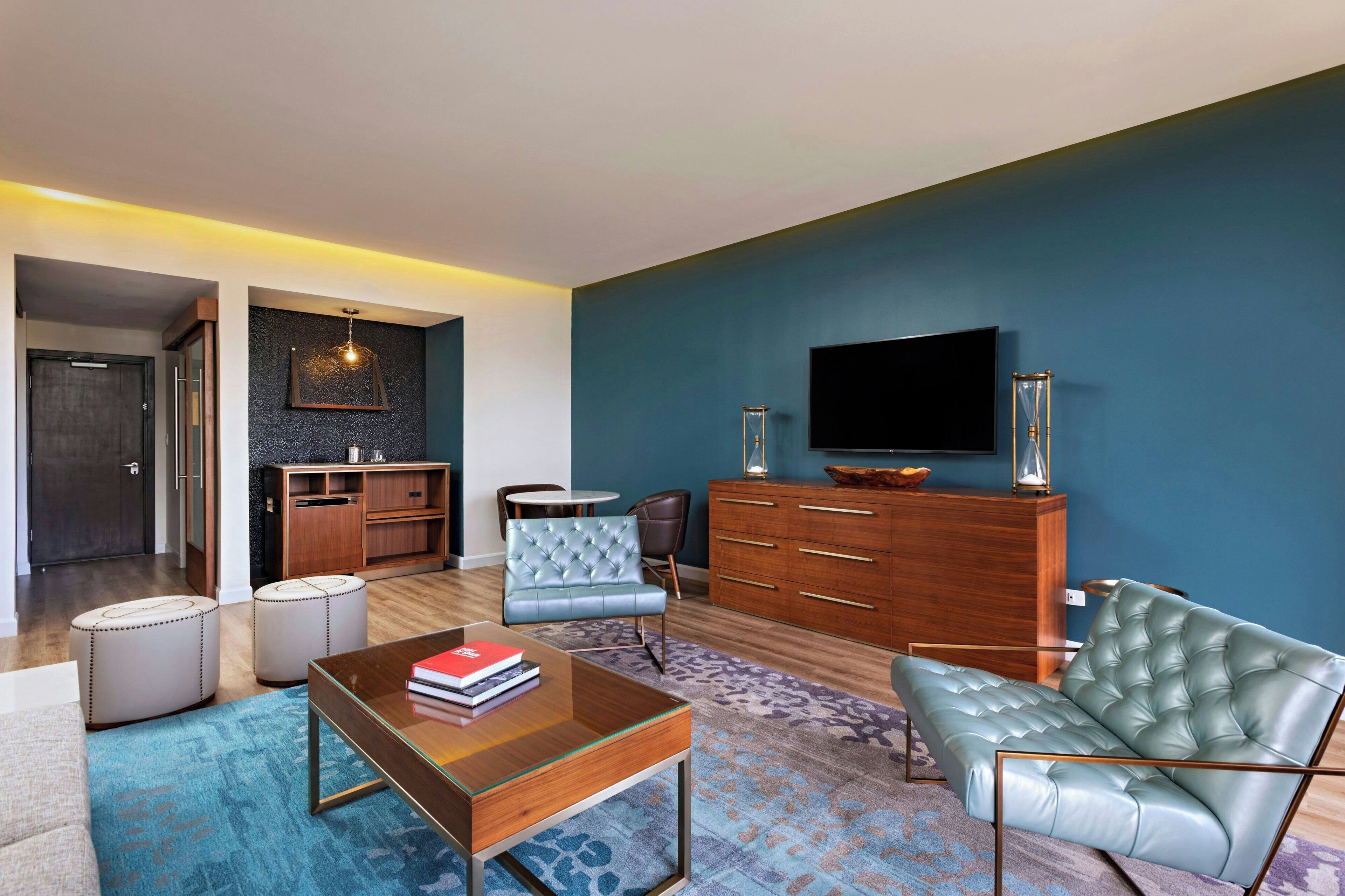Una sala de estar moderna con una pared azul de acento, un televisor de pantalla plana, un mueble de madera, un sofá capitonado y una mesa de centro.