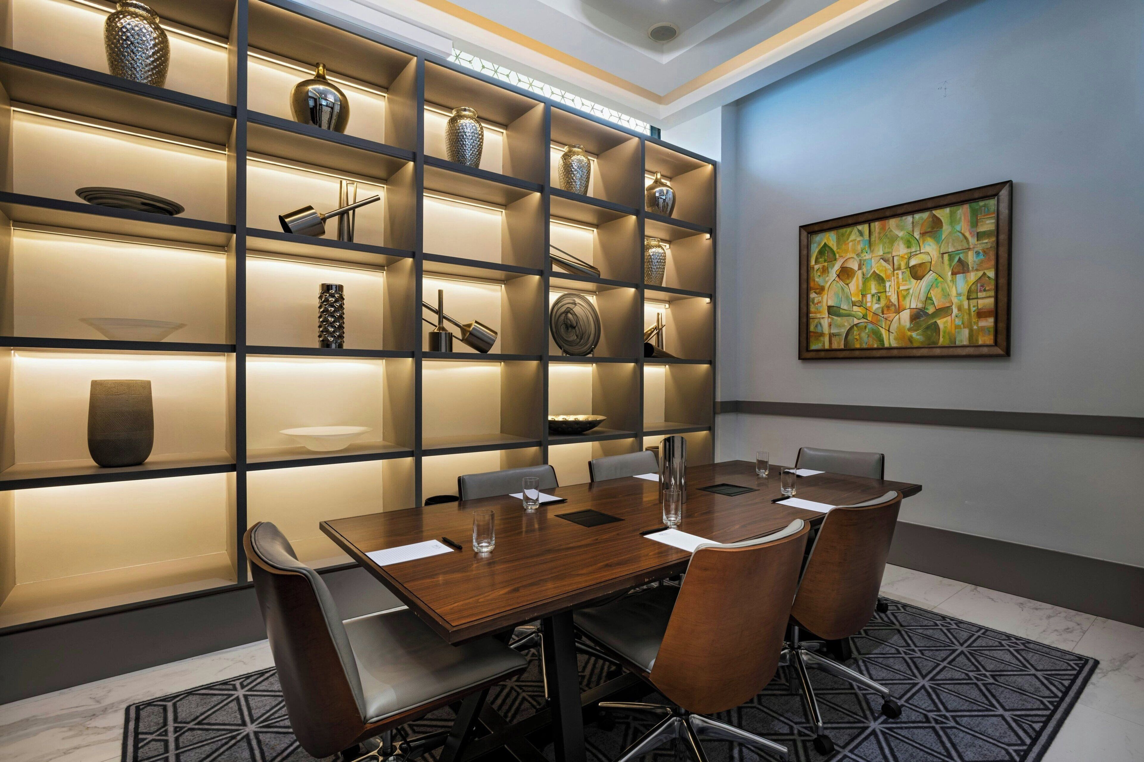 A conference room with a wooden table, chairs, and a wall-mounted shelf with decorative items.
