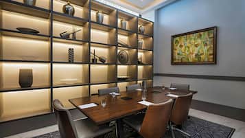 A conference room with a wooden table, chairs, and a wall-mounted shelf with decorative items.