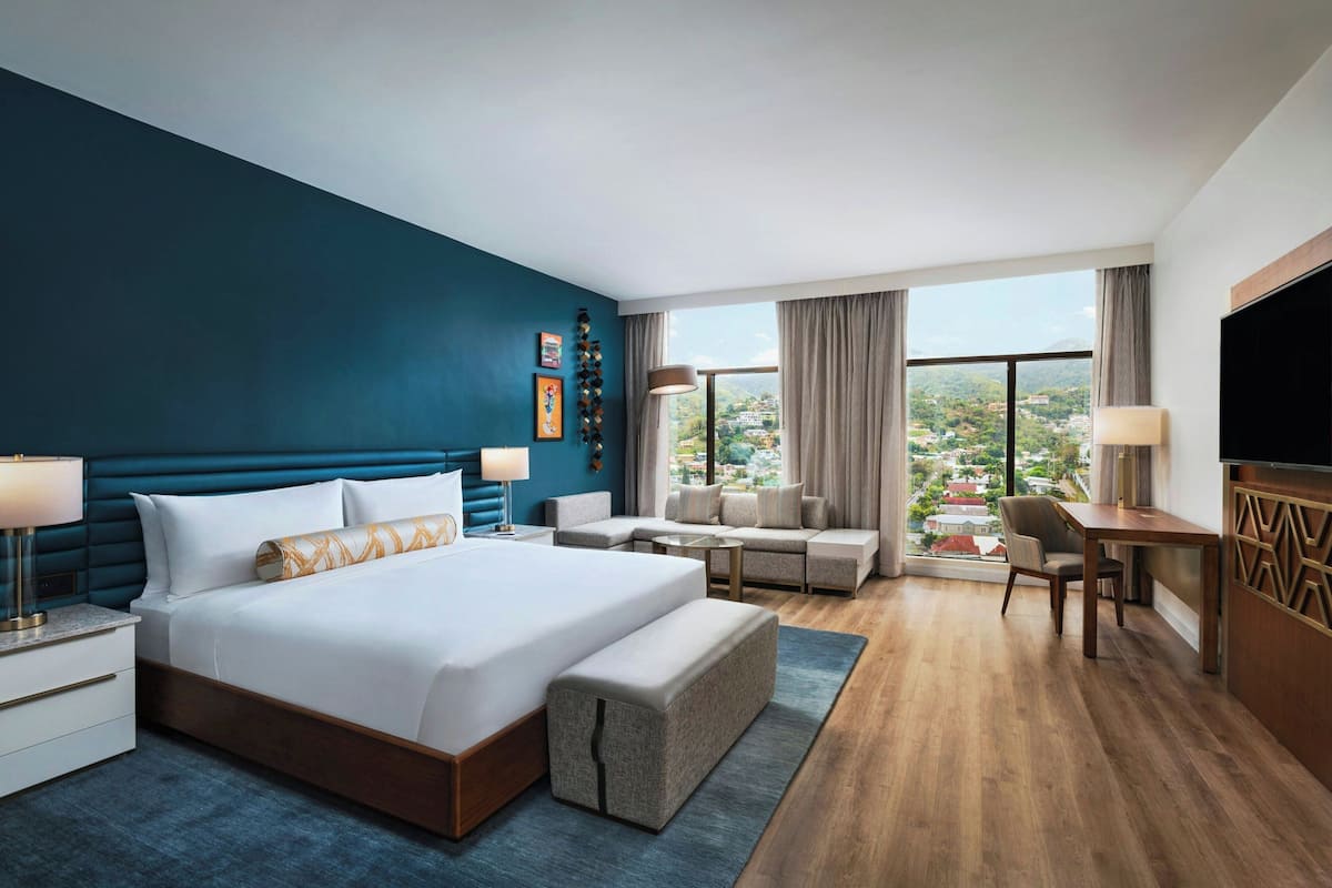 A modern hotel room with a large bed, a sofa, a desk, and a TV.