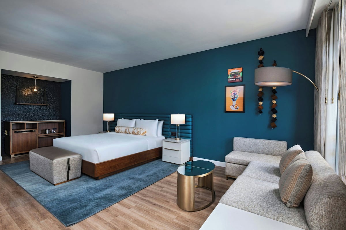A modern hotel room with a large bed, a sofa, a small table, and a desk.