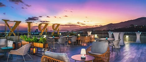Eine Dachterrasse mit Sitzgelegenheiten im Freien, Blick auf die Skyline der Stadt und einem Sonnenuntergang.