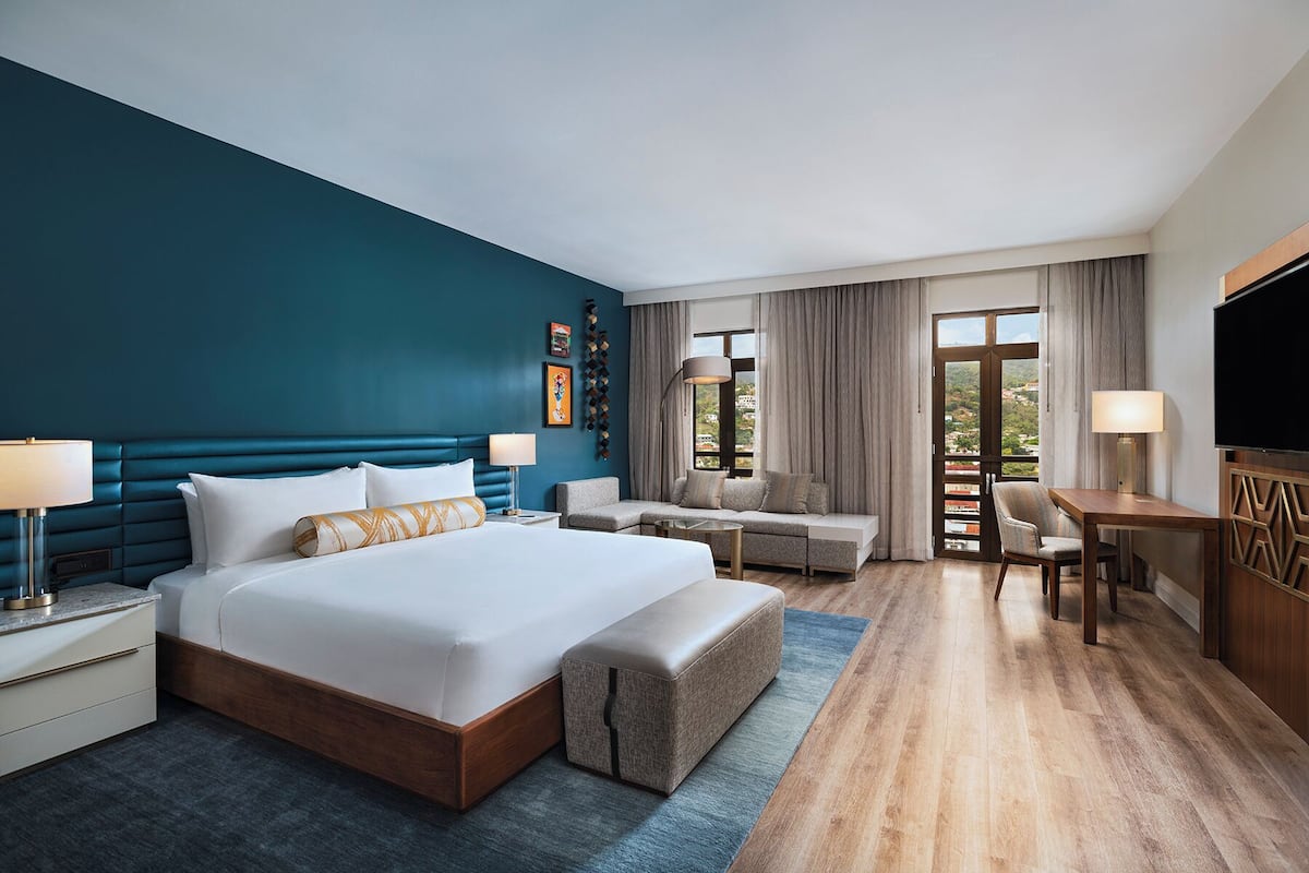 A hotel room with a large bed, a sofa, a desk, and a TV.