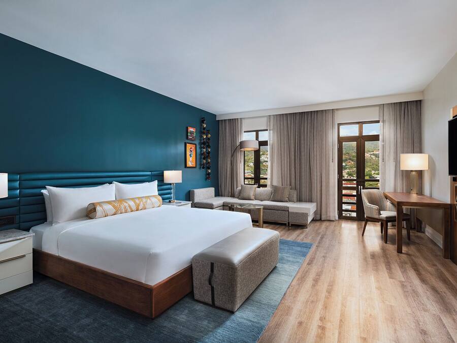 A hotel room with a large bed, a sofa, a desk, and a TV.