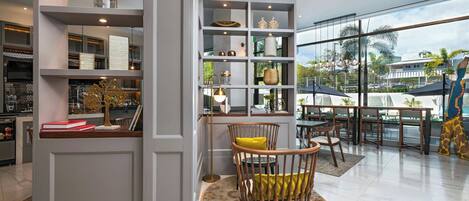 A modern interior with a large window, a round wooden chair with a yellow cushion, and a bookshelf filled with various decorative items.