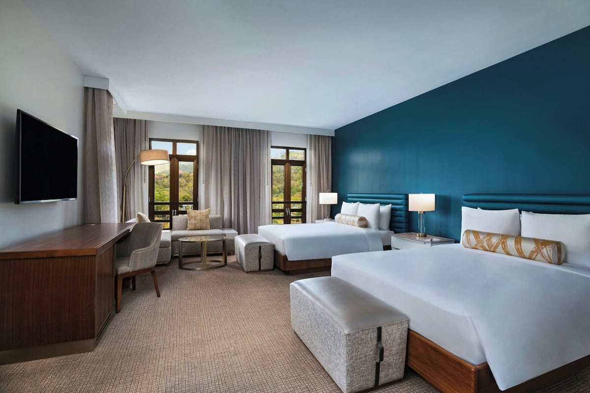 A hotel room with a large bed, a smaller bed, a desk, a chair, a sofa, and a TV.